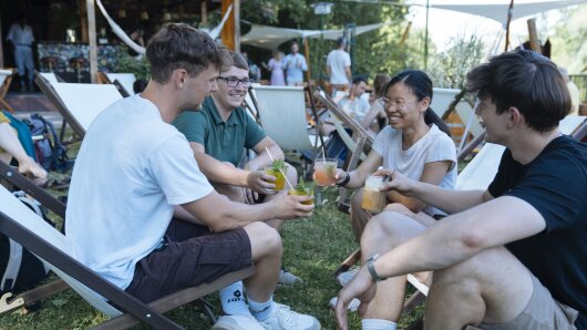 Personen sitzen im Grünen und stoßen mit einem Getränk an