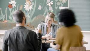 Eine junge Lehrerin sitzt einem Elternpaar gegenüber.