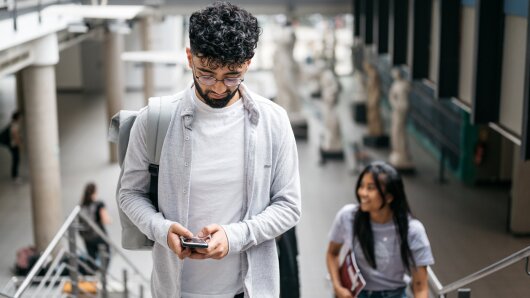 Person geht eine Treppe hoch und schaut dabei auf ein Handy