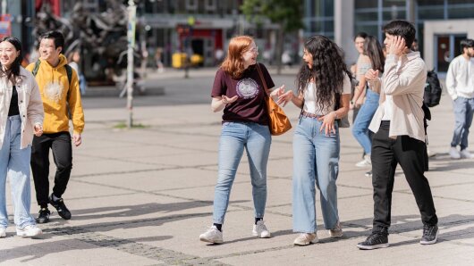Personen laufen über den Campus und unterhalten sich