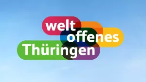 Der Claim »weltoffenes Thüringen« steht als buntes Logo vor blauem Himmel